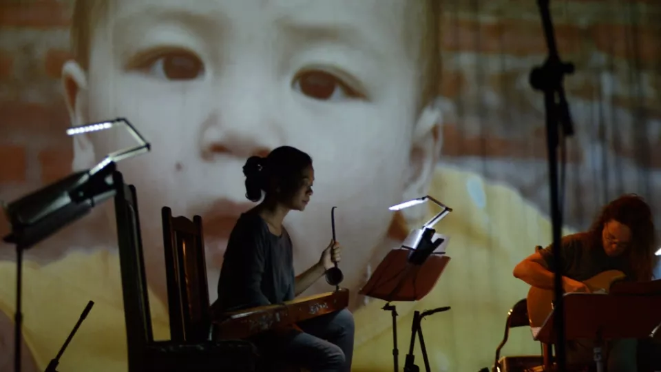 Föreställningsbild med instrumentalist i förgrund och projektion av bebis som fond. Foto
