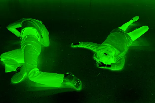 Foto: två personer i grön belysning som ligger på ett svart golv.