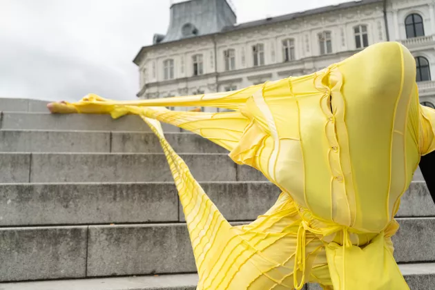 A person in fron of a staircase wearing a costume of yellow fabric. Photo.