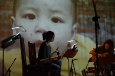 Föreställningsbild med instrumentalist i förgrund och projektion av bebis som fond. Foto