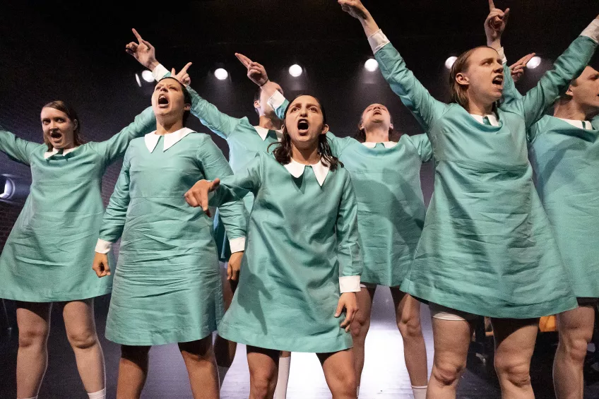 Flickor i turkos klänning sträcker upp armarna och sjunger.