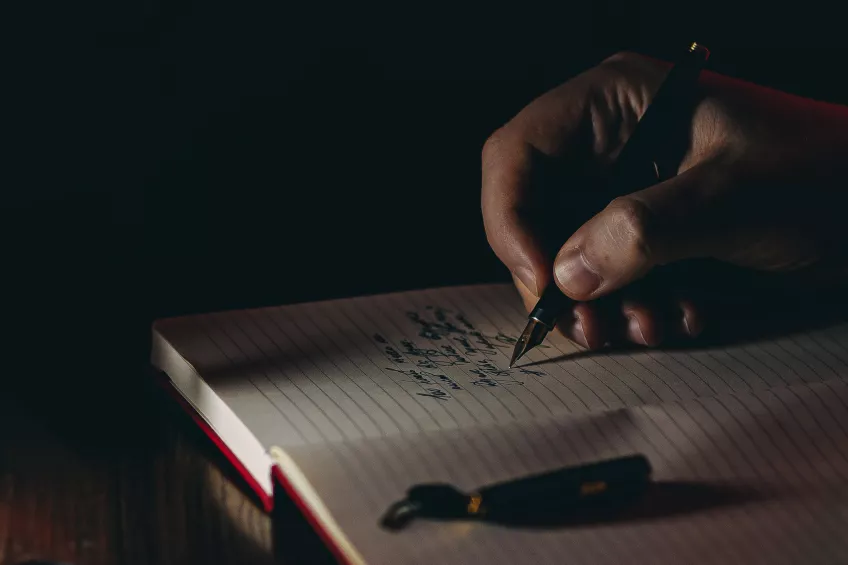 Närbild på hand som skriver i ett anteckningsblock. Fotografi.