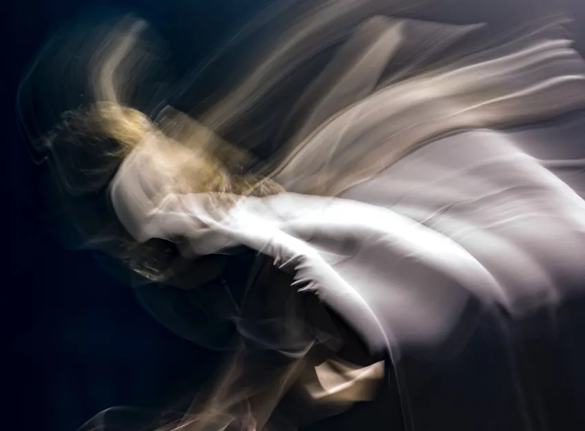 Abstrakt bild av person insvept i tyg i rörelse. Fotografi.