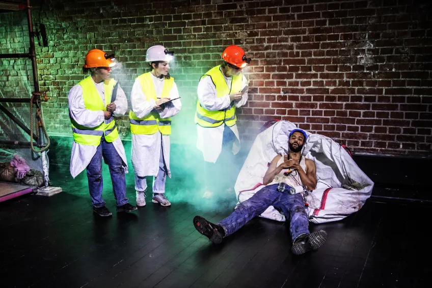 tre personer i varselväst och hjälmar tittar på en som ligger på en säck